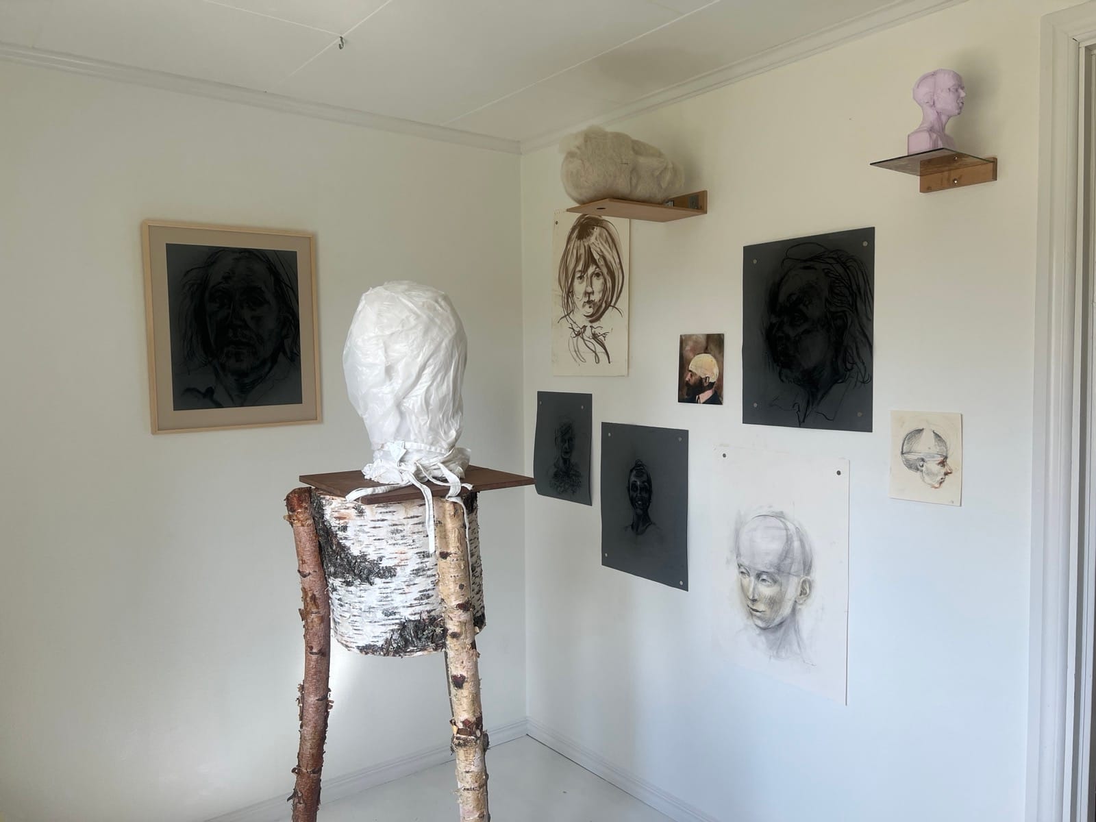 Gallerirummet på RUM44: teckningar och små skulpturer på väggen och ställningen med den inlindade figuren i förgrunden.
