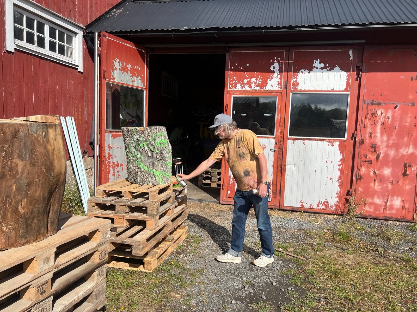 Kenneth Pils markerar stockens ändyta med grön sprayfärg framför ladugårdens röda portar.