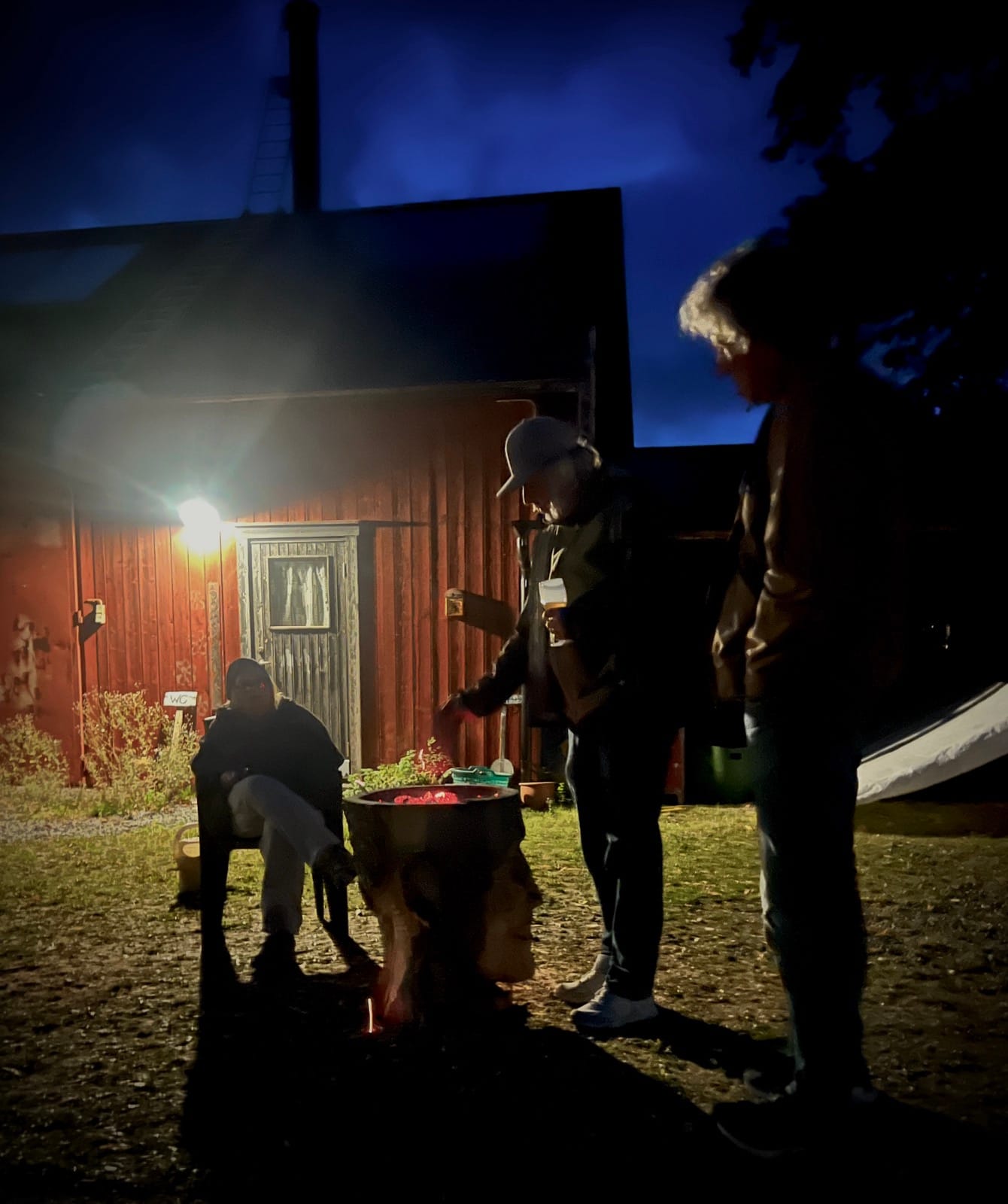 Kväll vid RUM44: besökare samlade vid elden, med skulpturerna i mörkret.