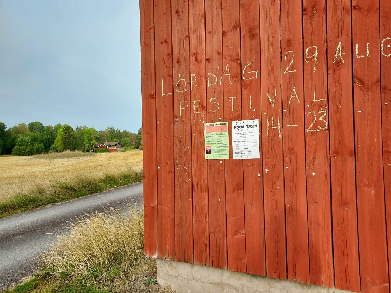 Krittexten ”LÖRDAG 29 AUG / FESTIVAL 14–23” på den röda plankväggen vid vägen till RUM44, bredvid affischerna för dagen.