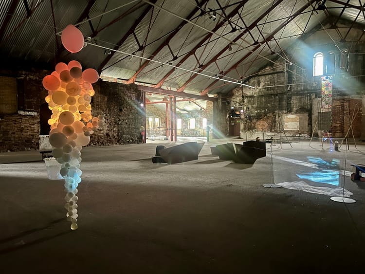 Översikt över Ånghammarens industrisal med ballongskulptur, färgade projektioner och en ljusstråle från taket.